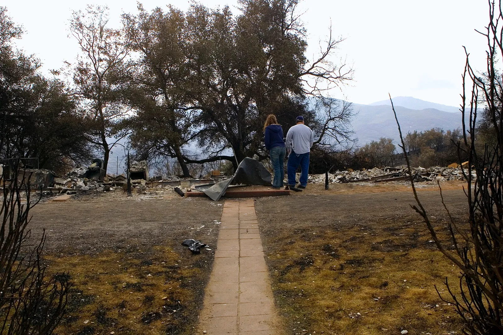 Two people standing among the burned remains of a home in California after a wildfire