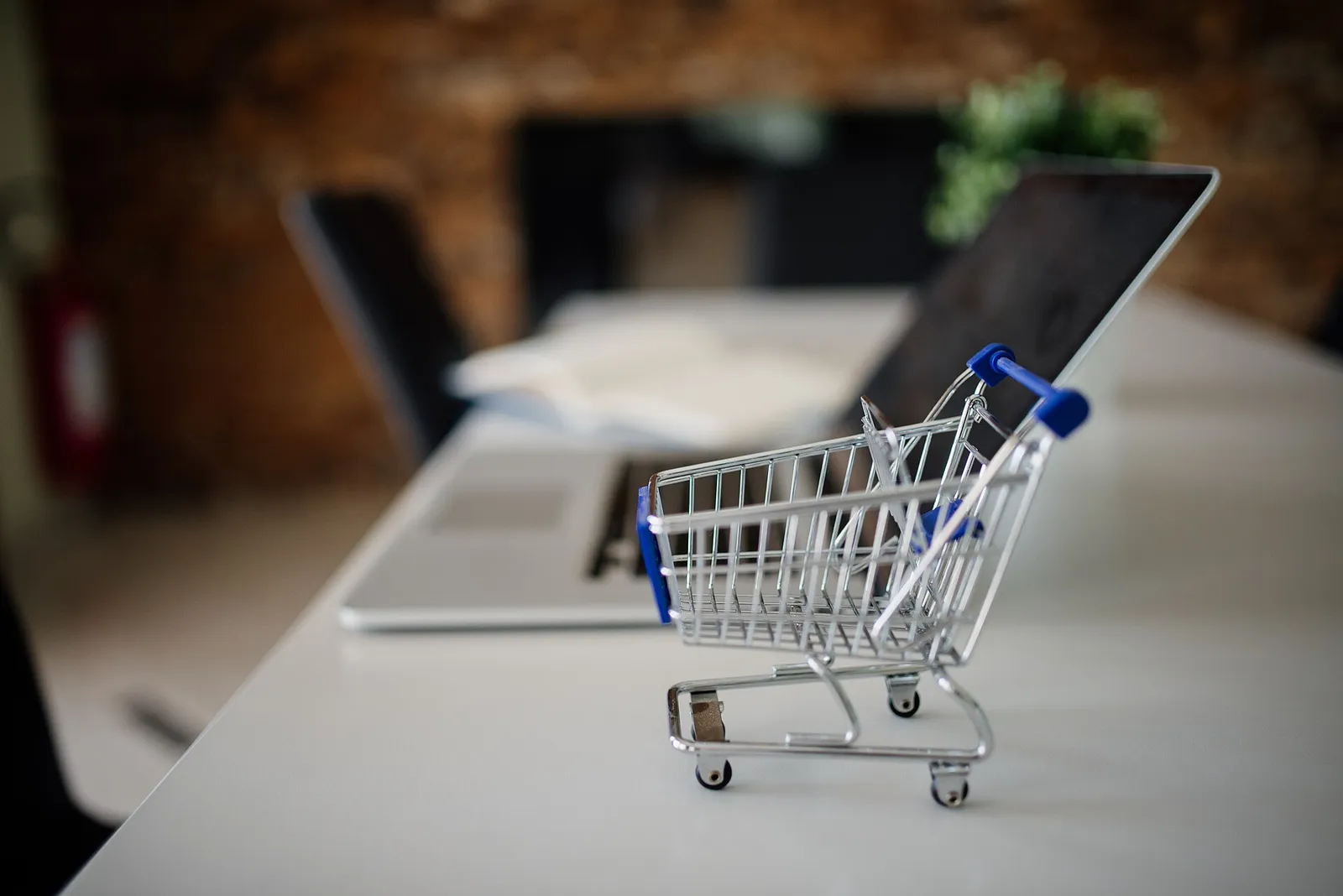 A miniature shopping cart beside a laptop, representing online retail
